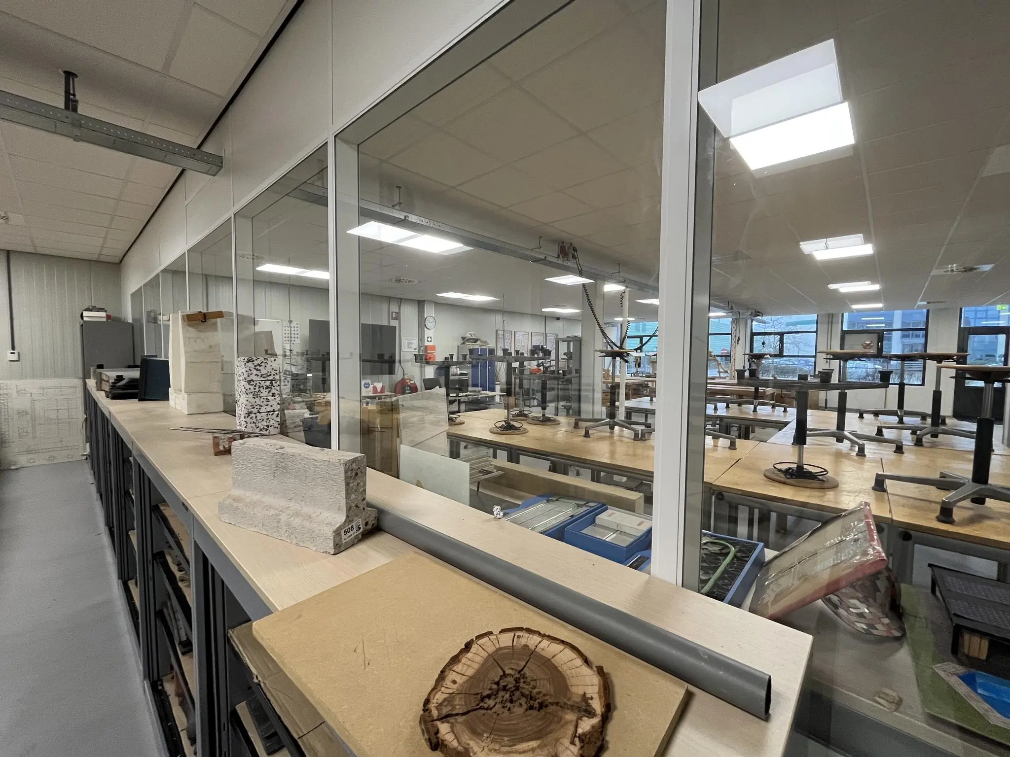 Kijk in een lege werkplaats of klaslokaal aan de Niels Bohrweg, met diverse bouwmaterialen en modellen op een kast en werkbanken met omgekeerde stoelen.